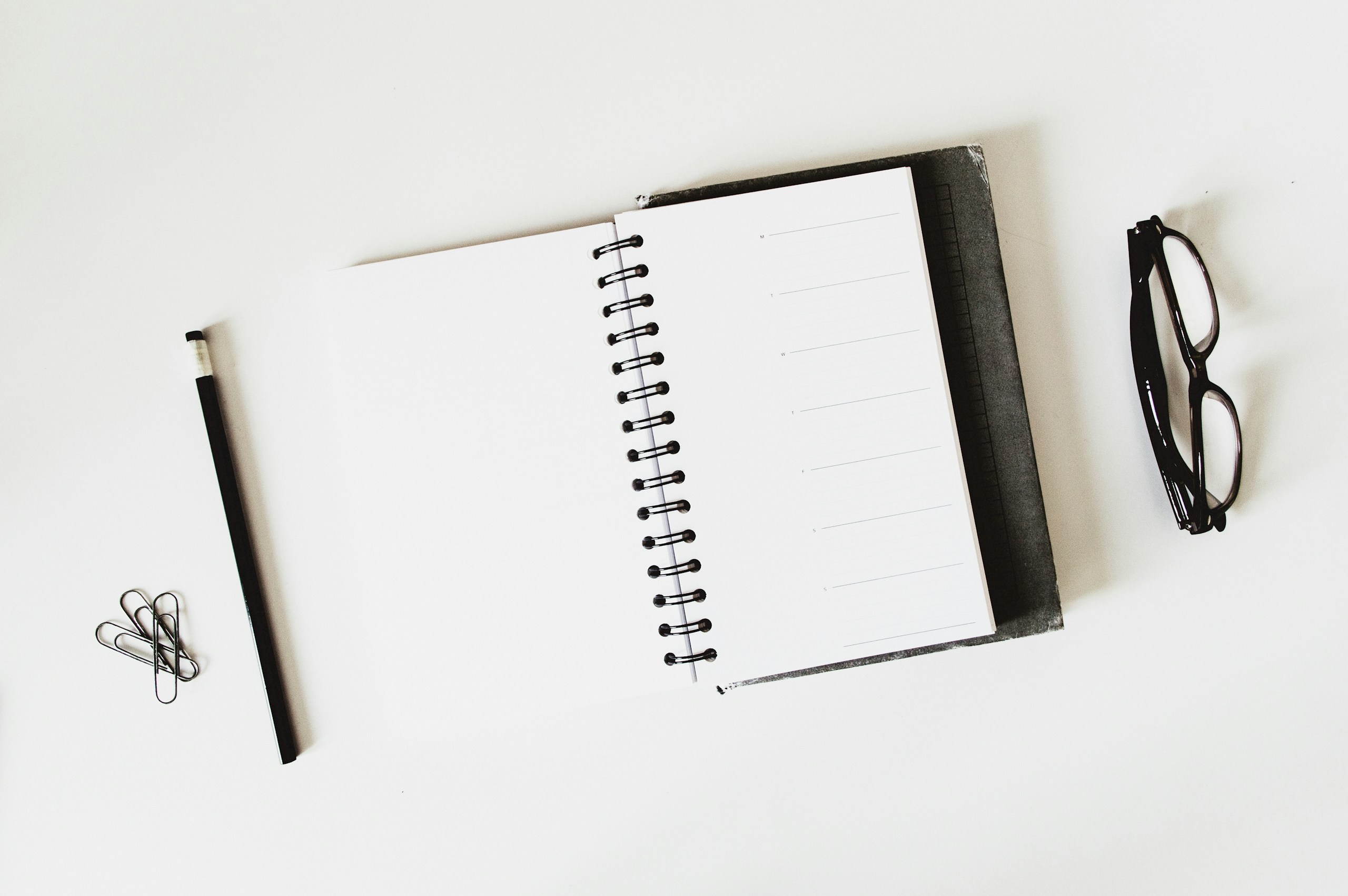 spiral notebook open beside a black pen on a white desk, ready for planning