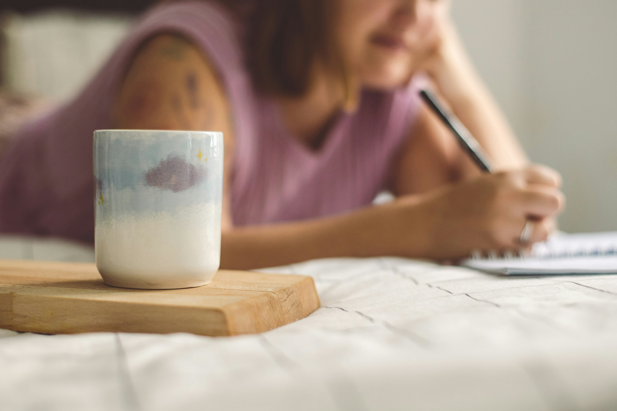 a woman writing on a notepad next to a coffee mug at her home desk in a morning light