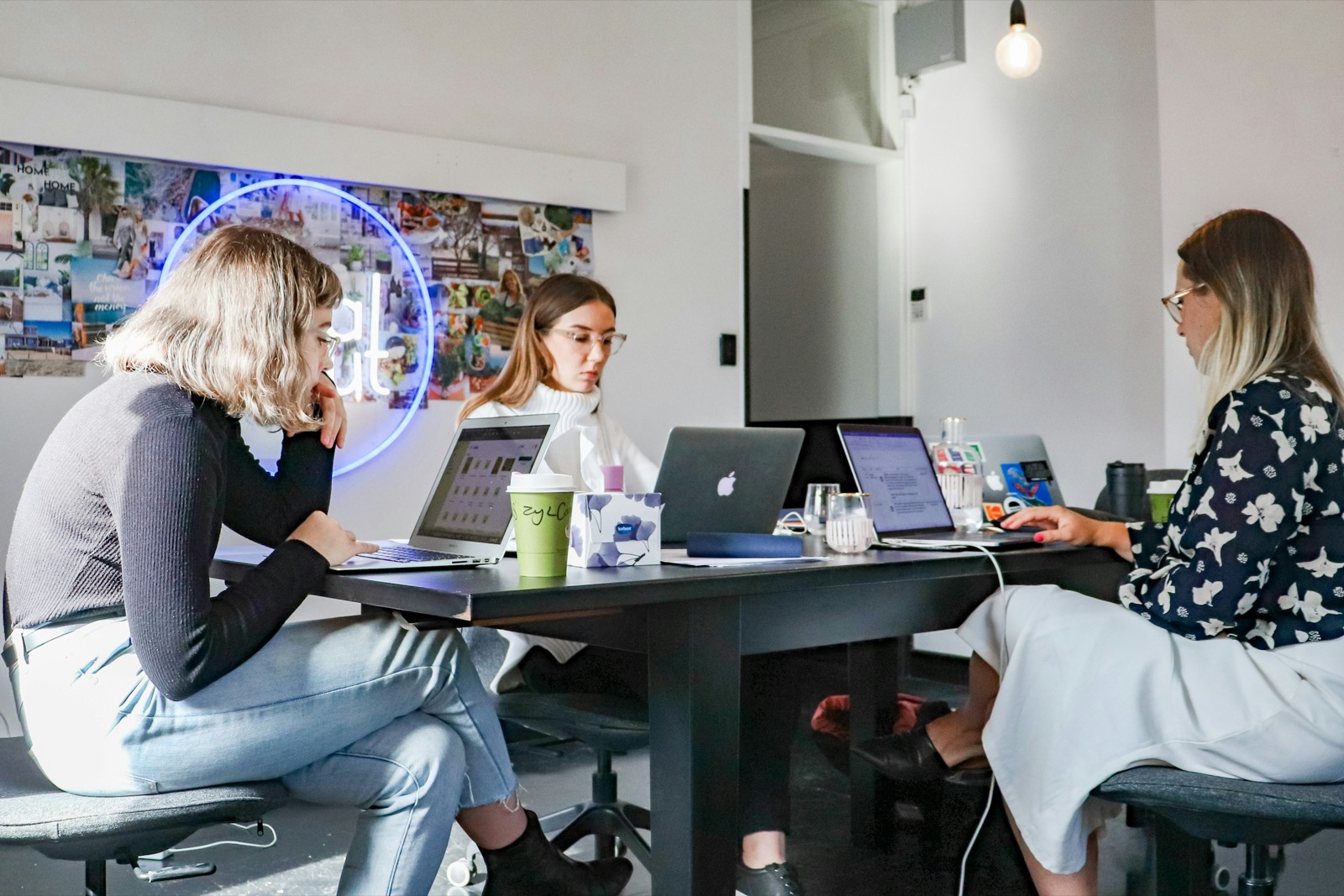 three women sitting facing each other at a shared work table, collaborating and focused